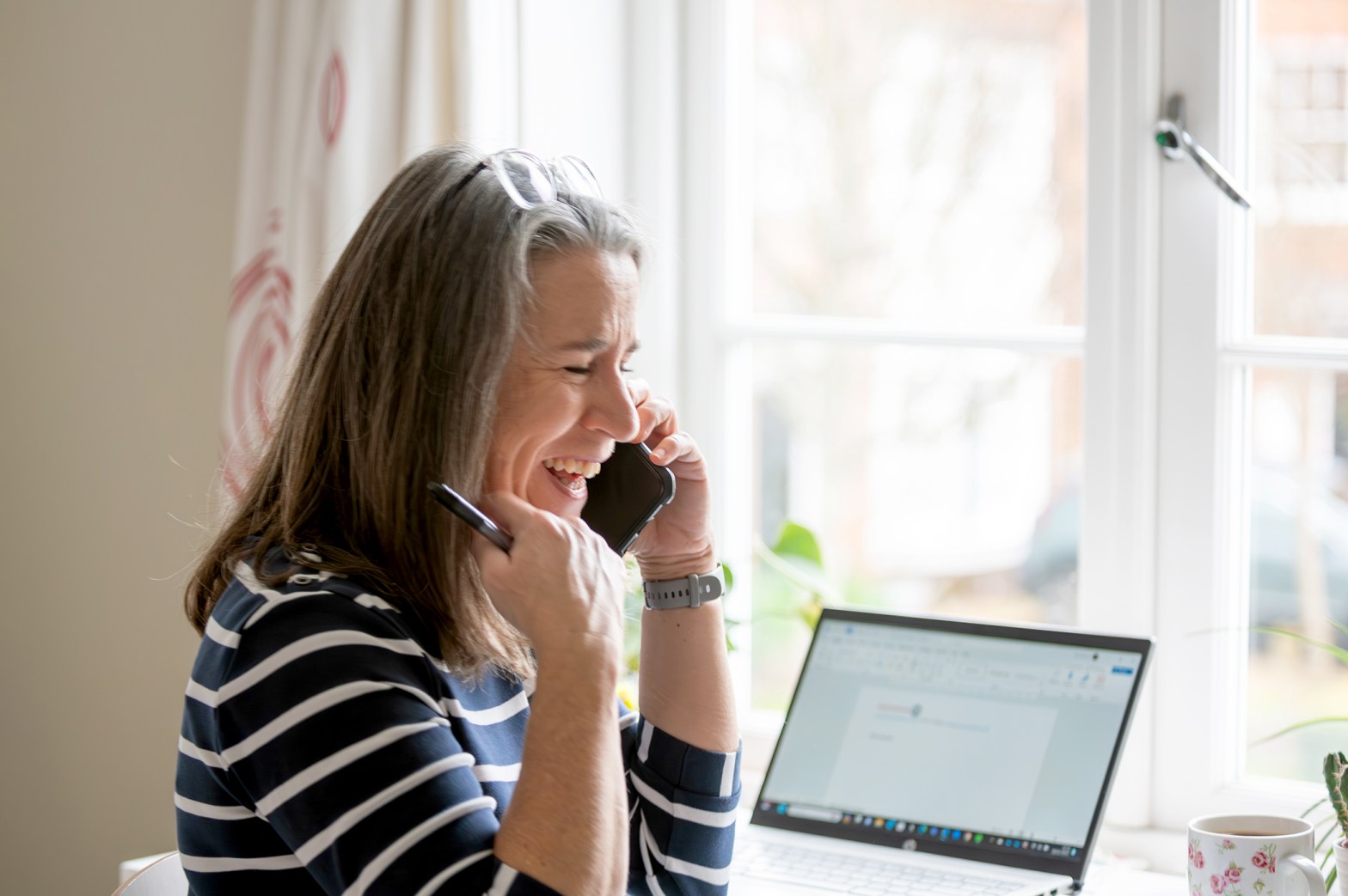 Image shows a woman laughing and talking while holding a mobile phone to one ear