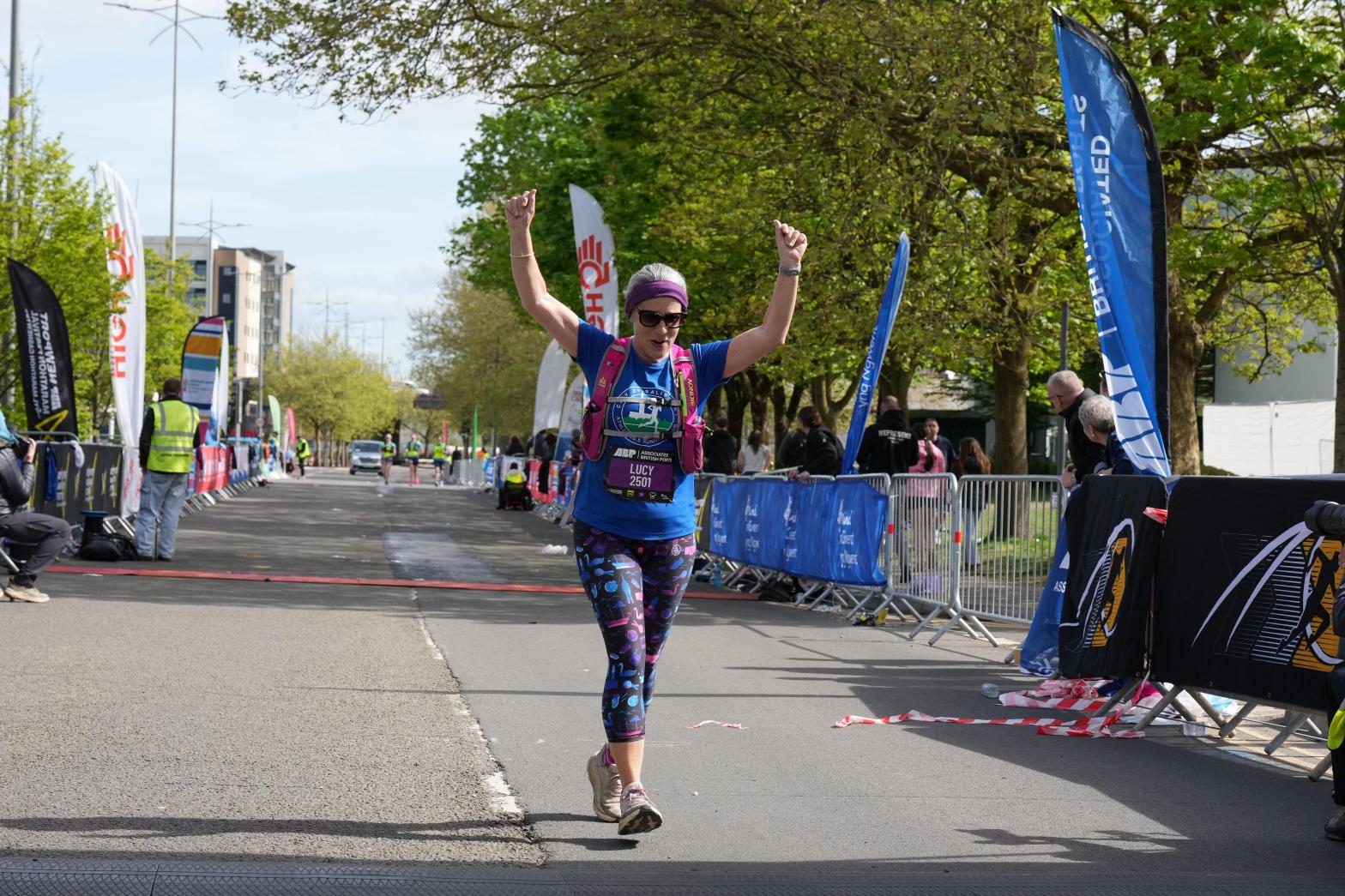 Image shows a woman in running gear smiling and raising her arms to the sky